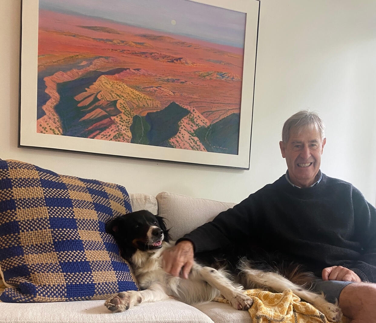 Clive Douglas at home with his dog, beneath one of his desert paintings