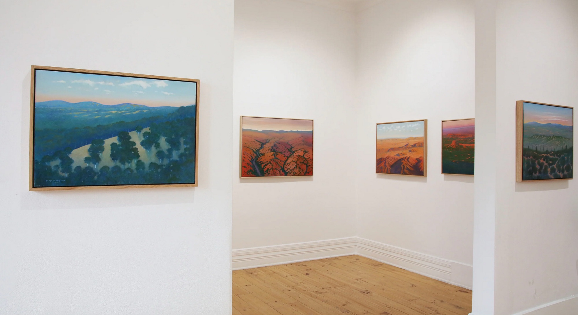 Clive’s paintings in pale oak frames around a white gallery room with a timber floor