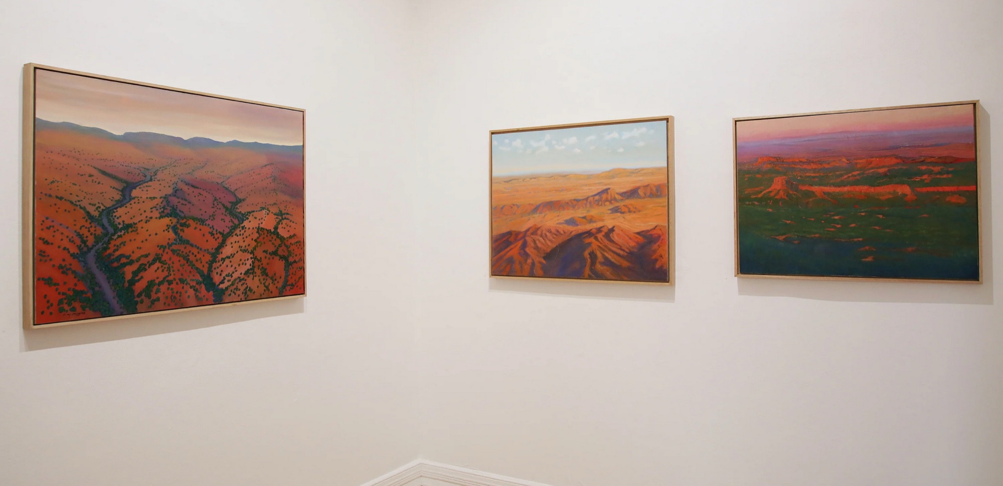 Three of Clive’s desert paintings in pale oak frames on a white gallery wall, Ancient Desert, N.T. in the centre